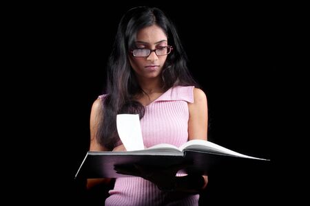 A beautiful Indian student checking notes before appearing for an exam, on black background.の写真素材