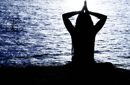 A silhouette of a hindu yogi traditionally praying on the banks of a river.の写真素材