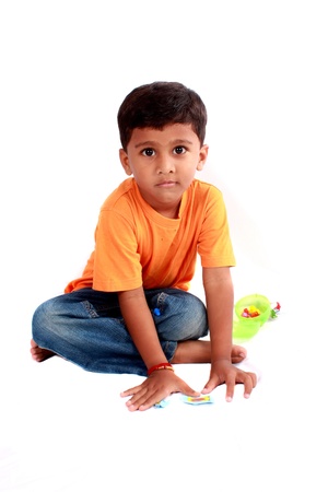 A cute Indian boy sitting on the floor, on white studio background.の写真素材