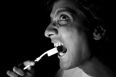 A man like a vampire brushing his teeth, in dramatic lighting.の写真素材