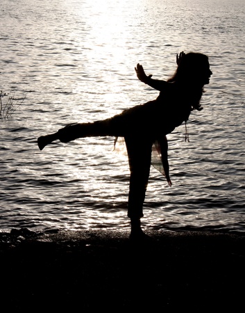 A silhouette of a female Indian yogi performing traditional yoga exercises near a river.の写真素材