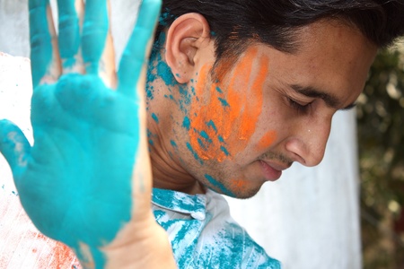 A young Indian man uses his hand to stop holi colors getting on to his face の写真素材
