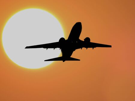 A silhouette of an airplane over a huge setting sun の写真素材