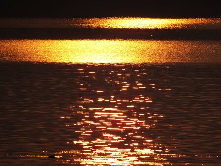 A backgrond of the water in a lake reflecting the bright golden sunlight                                の写真素材