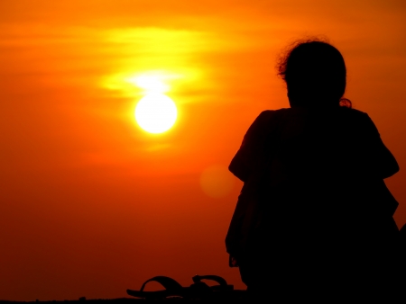 A silhouette of lonely woman sitting alone watching the sunset.の写真素材