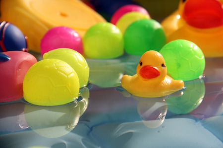 A yellow baby duck toy floating in water along with colorful balls in a baby swimming poolの写真素材