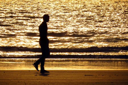 A lonely man taking a walk on the beach in the eveningの写真素材