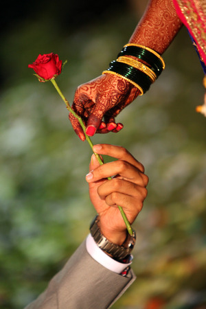 A groom offering a red rose to his bride whose hand is beautifully decorated with traditional bangles and mehendiの写真素材