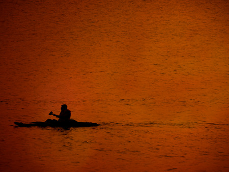 A silhouette of a man kayaking in a lake during his summer holidays in the evening dusky light.の写真素材