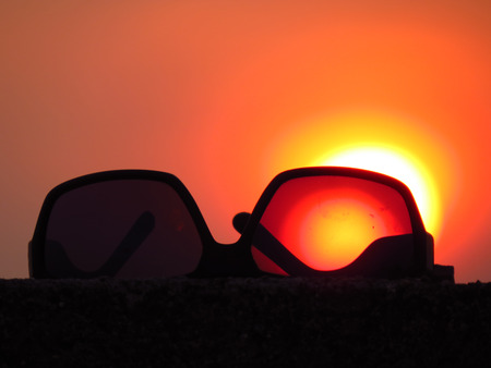 A metaphorical image of sunglasses against a setting orange sun during summer holidays