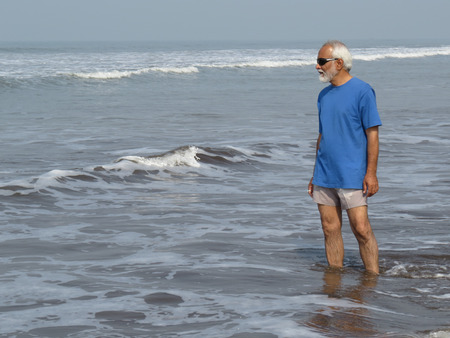 An elderly Indian man feeling young and contemplating his younger days on his holidays on the beach.の写真素材