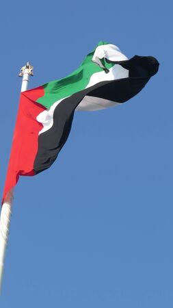 A huge flag of United Arab Emirates - UAE  fluttering in the wind, against clear blue skies.の写真素材