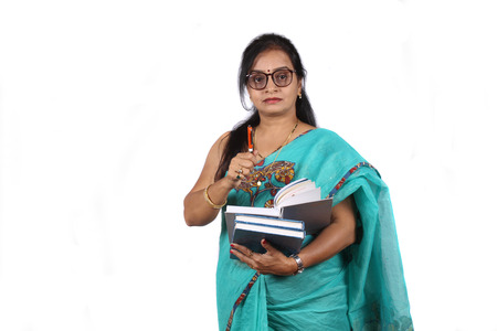 An Indian teacher with a book and pen giving explanation, on white studio background.の写真素材