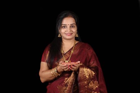 A beautiful middle aged Indian woman holding a lamp in her hand, on black studio background.の写真素材