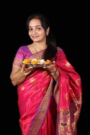 A beautiful Indian Indian woman holding a hindu ritual plate, on black studio background.の写真素材