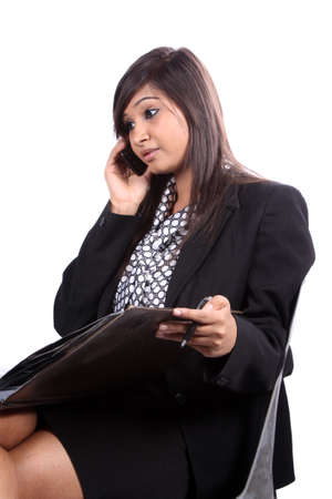 A young beautiful Indian female executive talking on the phone, on white studio background.の写真素材