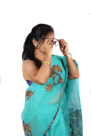 A middleaged Indian woman with eyesight problem wearing her glasses, on white studio background.の写真素材
