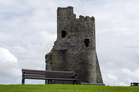 An empty wooden bench in the foreground with a castle ruin in the background の写真素材