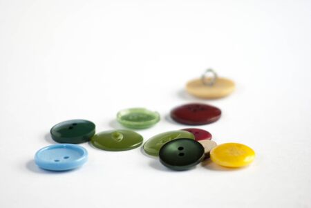 A variety recycled buttons of different colours and sizes, scattered on a white background の写真素材