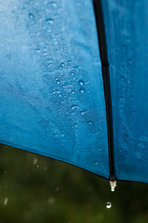Rain runs and drips from the edges of the blue umbrella illuminated by the sun in a sudden downpour の写真素材