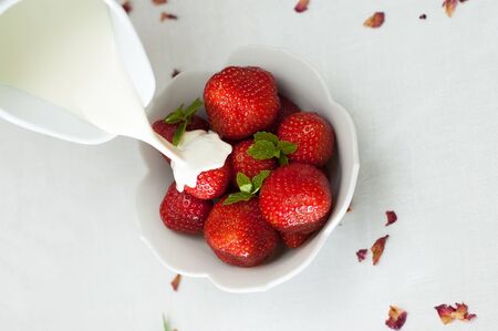 Rich cream delicately poured over bowl of fresh vibrant straberrys with a few sprinkled new mint leaves.の写真素材