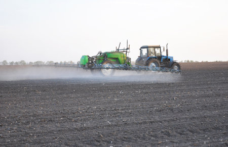 KIEV - UKRAINE, APRIL - 20, 2017: Tractor fertilizer tank with fertilizer from the sprinkler spray. Tractor Mounted Tank Sowing and Plowing action on the corn field in spring sunset.のeditorial素材