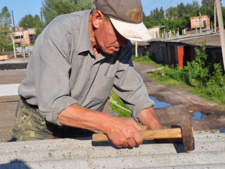 KIYV, UKRAINE - JUNE, 6, 2017: Roofer repair asbestos roof with hammer. Old contractor roofing construction.のeditorial素材