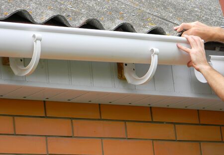 Contractor installing plastic roof gutter. Plastic Guttering, Rain Guttering & Drainage by Handyman hands.の写真素材