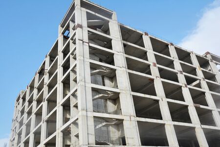 Incomplete residential building construction with new apartments against cloudless blue sky. 