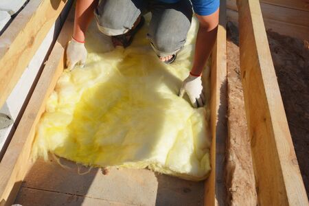 A building contractor is applying mineral wool thermal insulation under the sheathing, between roof...