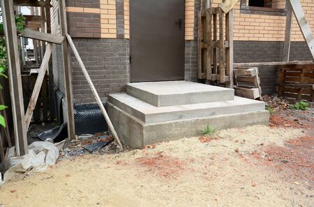 Building poured concrete front porch steps to the entrance door of a brick house under construction.