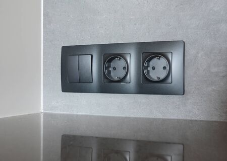 A close-up on black European socket, power outlet plug and light switch on a gray wall in the kitchen.の写真素材