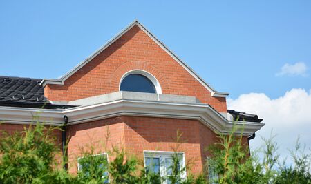 A close-up on a brick house facade with a cornice, decorative molding and attic round window under...