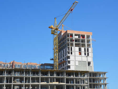 Construction of a new office building, shopping center, mall with a tower crane against blue sky.