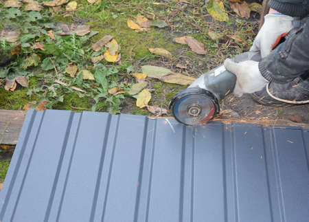 Constructing a roof a building contractor is cutting, making shorter a metal corrugated roof tile or...