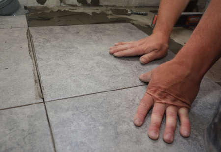 House renovation: a close up of floor ceramic tiles installation. Gray square non-slip floor tiles...