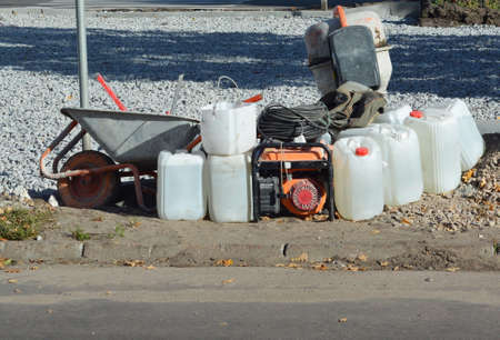 A portable backup generator with a concrete mixer machine, a wheel barrow, and plastic jugs with...