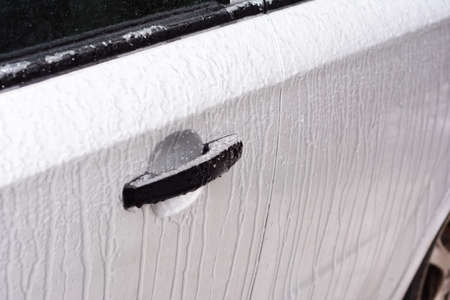 De-icing car doors and locks. A close-up of a frozen lock of a car door after freezing rain, ice storm weather in winter.の写真素材