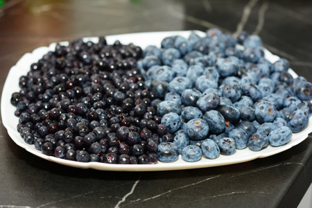 Blueberries and bilberries on the white plate. Ripe bilberries are smaller and darker than blueberries.の写真素材