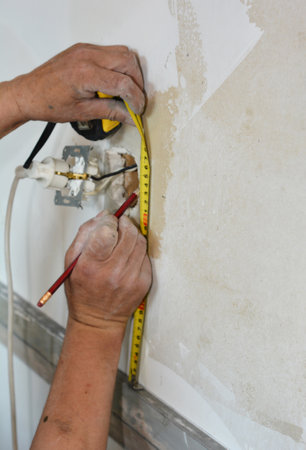 Tiling around electrical outlets over drywall. A man is taking measures carefully to tile around an electrical socket.の写真素材