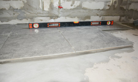 A close-up on large square natural stone, soap stone slip resistant bathroom tiles installation on a bathroom floor using a spirit level.の写真素材