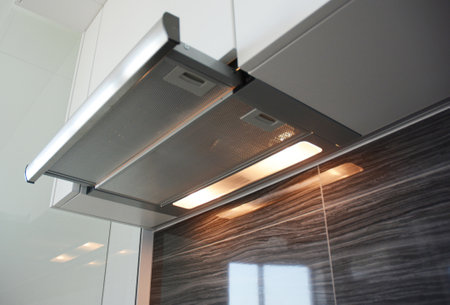 A close-up on a built in, integrated into kitchen cabinet stainless steel range hood, cooker hood, exhausted or extractor vent hood working with lights on in the kitchen.の写真素材