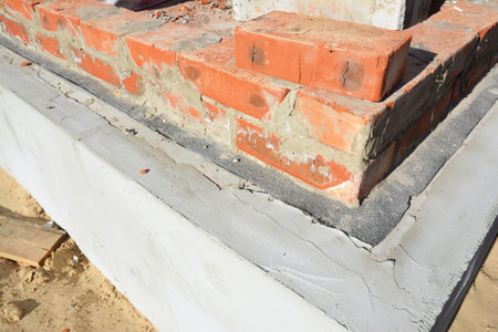 Laying a brick wall above the insulated foundation with a damp-proof waterproofing bitumen membrane to protect the foundation from water leaks.の写真素材