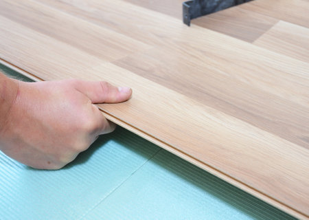 Contractor installing wooden laminate flooring with insulation and soundproofing sheets.の写真素材
