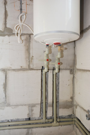 Installation of an electric boiler and installation of plastic pipes into grooves cut in the wall. Electric boiler with hot and cold water pipes.の写真素材
