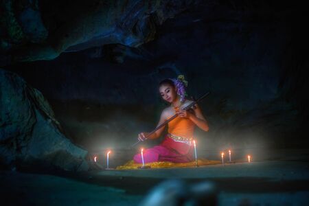 fine art portrait of thai woman wearing Thai dress playing thai An alto fiddle on rock backgroundの写真素材