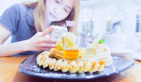 Woman taking photo of her cake in cafe with smart phoneの写真素材