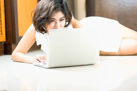 happy asia woman lying on floor with the laptop at homeの写真素材