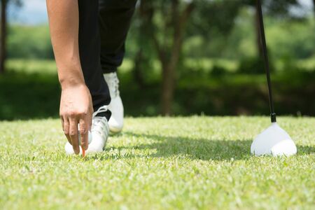 Golfer placing golf ball on tee on a sunny day at the golf courseの写真素材