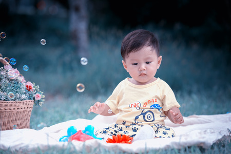 Asia Baby boy sitting on green grass in the park with soap bubblesの写真素材